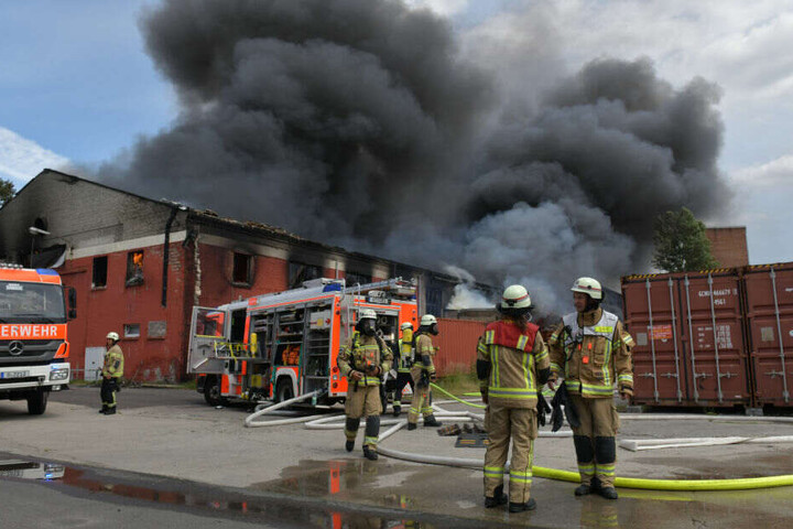 Feuerwehrleute stehen vor der Lagerhalle.