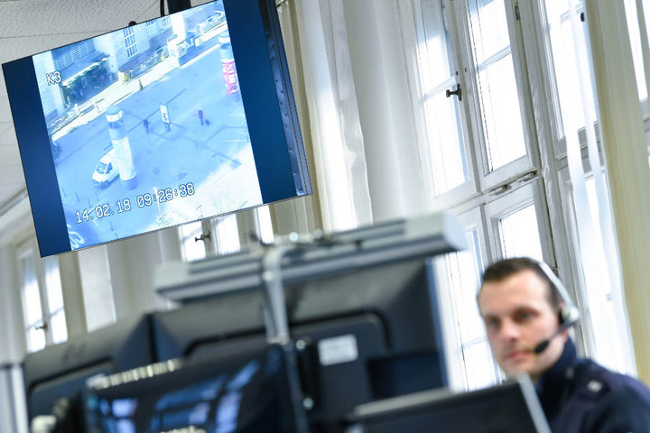 Ein Polizist sitzt im Februar 2018 im Führungs- und Lagezentrum an seinem Arbeitsplatz in Mannheim. Im Hintergrund hängt ein Monitor, auf dem das Bild einer Überwachungskamera am Hauptbahnhof zu sehen ist.
