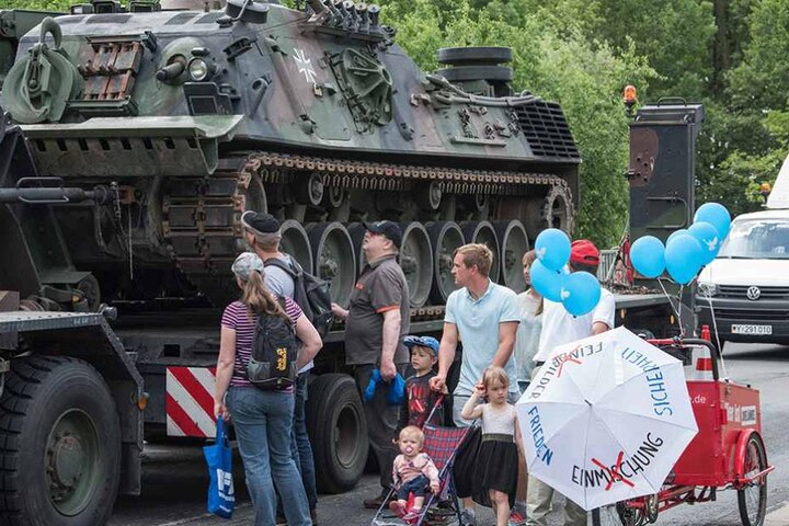Ein Mitglied der Partei Die Linke protestiert beim "Tag der Bundeswehr" für Frieden neben einem Bergepanzer.