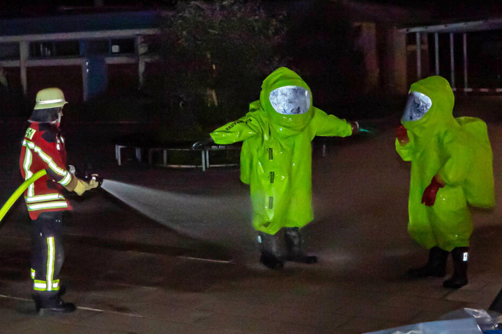 Einsatzkräfte in Schutzkleidung werden abgespritzt.