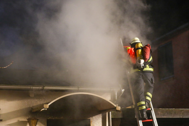 Ein Feuerwehrmann steht auf der Leiter und versucht den Brand am Dach zu bekämpfen.