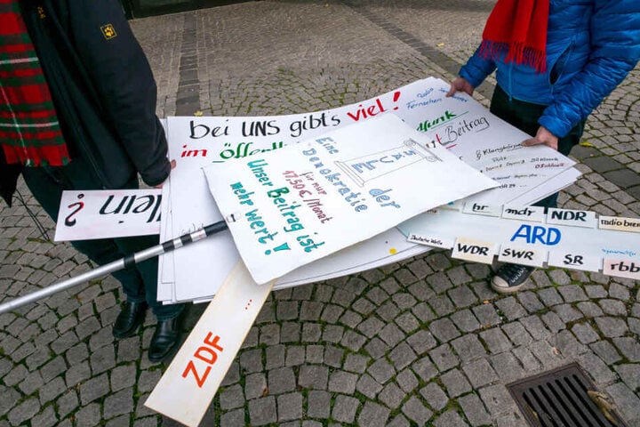 Diverse Protestplakate werden von zwei Männern vor das Funkhaus des Bayerischen Rundfunk (BR) getragen.