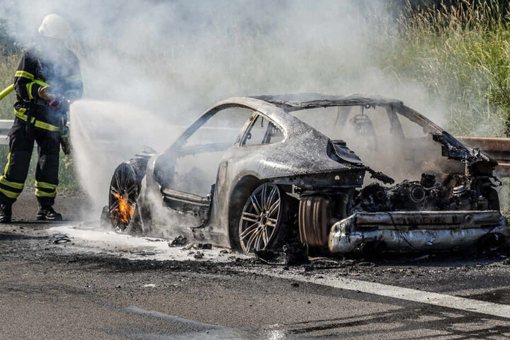 Ein Feuerwehrmann löscht den brennenden Porsche.