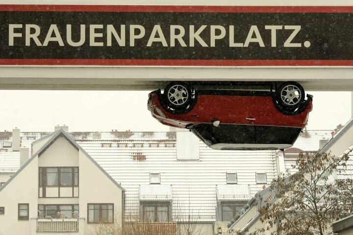 Ein Auto hängt verkehrt herum an einem Durchgang in München: Über der Installation, die für einen Autohersteller wirbt, steht provokant die Aufschrift "Frauenparkplatz".