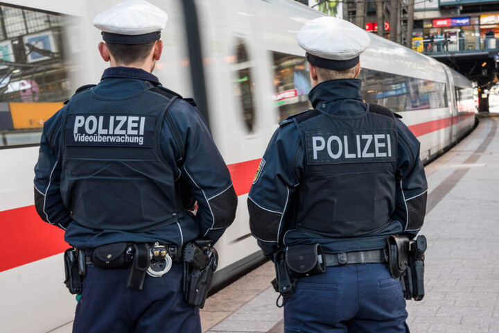 Zwei Bundespolizisten stehen am Bahnhof, während ein ICE vorbeifährt.
