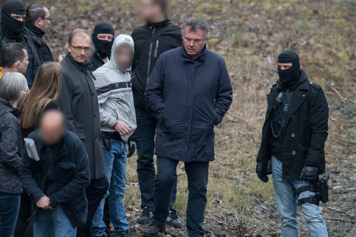 Ali B. bei der Tatortbegehung am 27.03.2019 flankiert von mehreren maskierten Polizeibeamten.