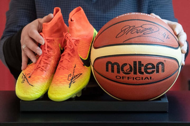 Mitarbeiterin des Auktionshauses Eppli präsentiert die handsignierten Schuhe von Mario Götze und den Basketball von Dirk Nowitzki.
