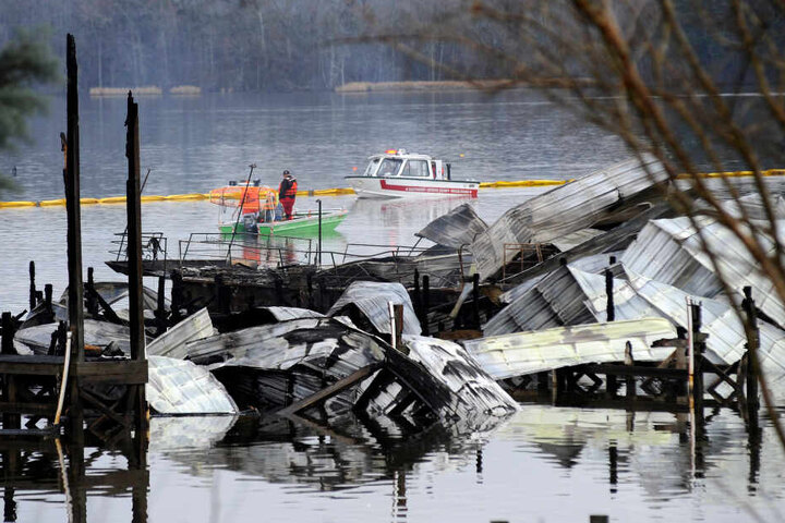 Ein Boot patrouilliert in der Nähe der verkohlten Überreste des bei einem Brand zerstörten Docks und mehrerer Hausboote.