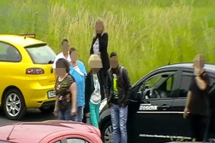 Der "Verletzte" steht neben dem Auto, während der Fahrer (re.) telefoniert, um Hilfe zu rufen.