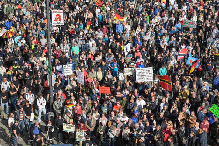Viele Demonstranten stehen mit Transparenten und Fahnen auf einem Platz vor der Stadthalle von Cottbus und protestiert gegen Zuwanderung und die Asyl-Politik der Bundesregierung.
