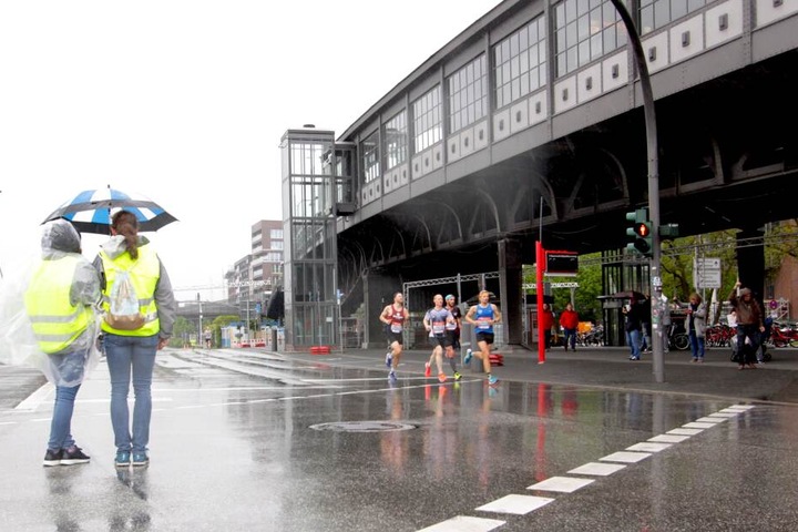 Zwei Helferinnen beaufsichtigen, mit Regenschirmen ausgestattet, die Marathonstrecke auf der Höhe des U-Bahnhofs Baumwall.