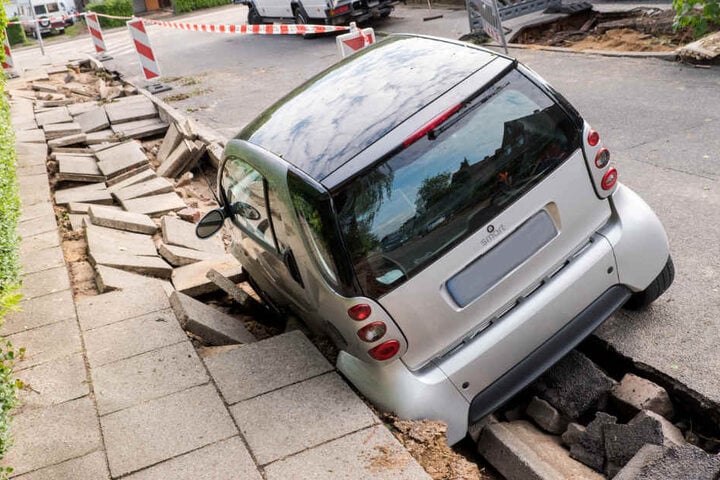 Nach der Überflutung steckt ein Auto in der abgesackten Straße fest.