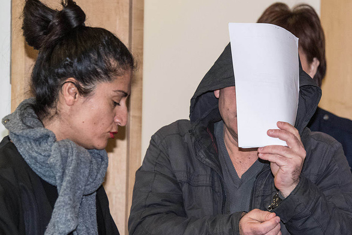 Der Angeklagte im Schleuser-Prozess hält sich Papier vor das Gesicht und kommt in Handschellen in den Verhandlungssaal des Amtsgerichtes, links seine Anwältin Mehtap Ayhan.