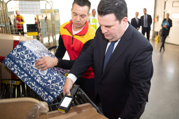 Hubertus Heil (SPD, r) scannt ein Pateket zusammen mit einem Paketboten ein.