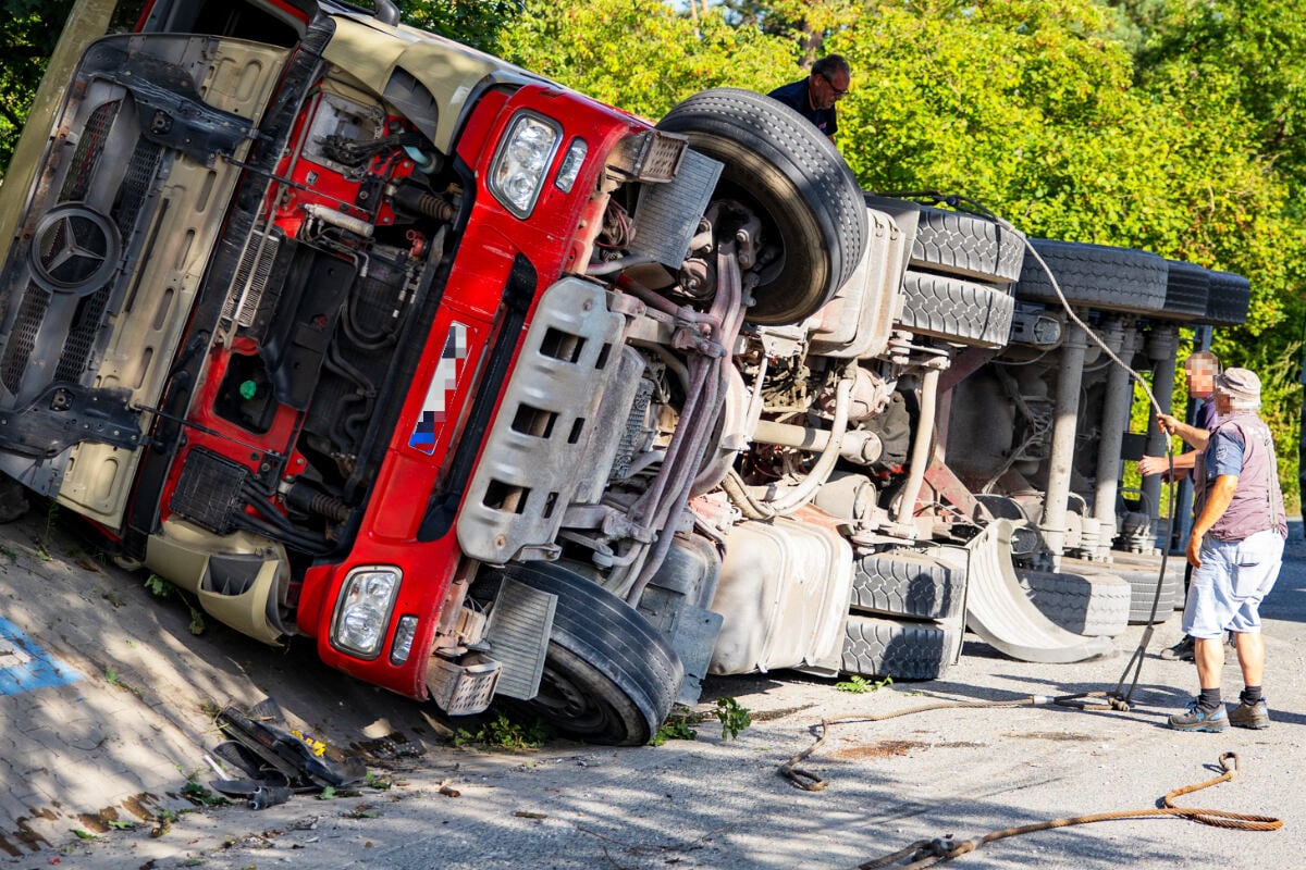 Lastwagen bleibt an Brücke hängen und kippt um: Fahrer verletzt