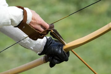 Mann zielt auf Sportplatz mit Pfeil und Bogen auf mehrere Kinder