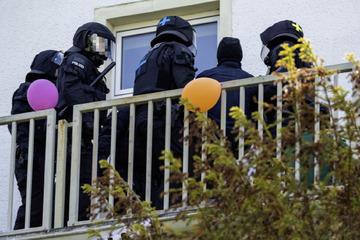 Polizisten mit Helmen und Schlagstöcken dringen in mit Luftballons dekoriertes Haus ein