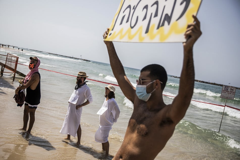 Israel, Tel Aviv: Demonstranten stehen am Strand im Rahmen eines Protests gegen weitere Covid-19-Maßnahmen.