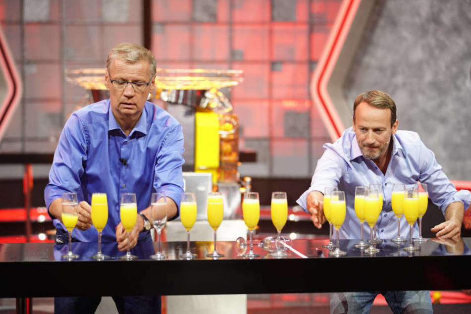 Wer ist schneller? Günther Jauch und Wotan Wilke Möhring sollen möglichst fix Gläser mit Orangensaft füllen und auf einen Tisch stellen.