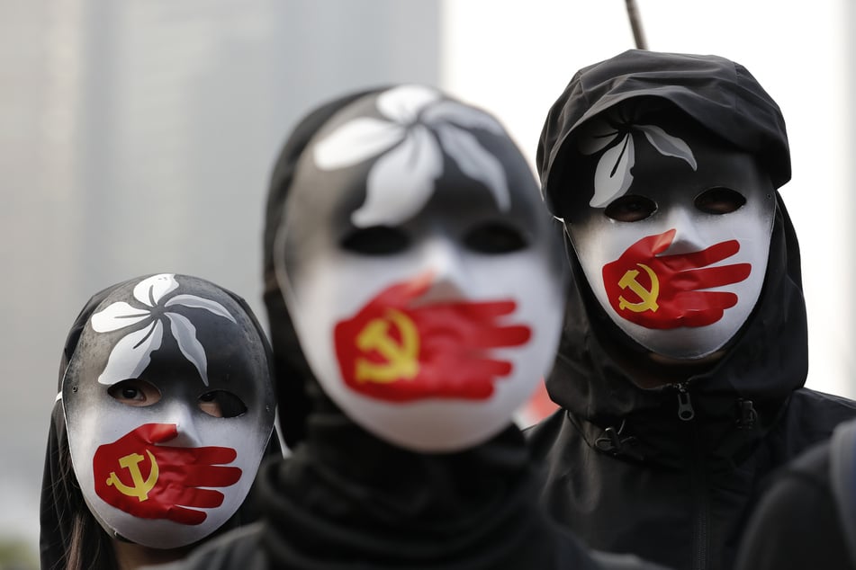 Pro-demokratische Demonstranten tragen Masken. Sie protestieren gegen den Umgang Chinas mit der muslimischen Minderheit der Uiguren und den zunehmenden Einfluss der autoritären kommunistischen Führung China.