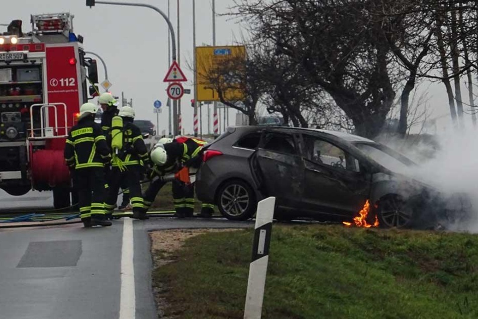 Flammen schlagen aus dem neben der Straße abgestellten Auto.