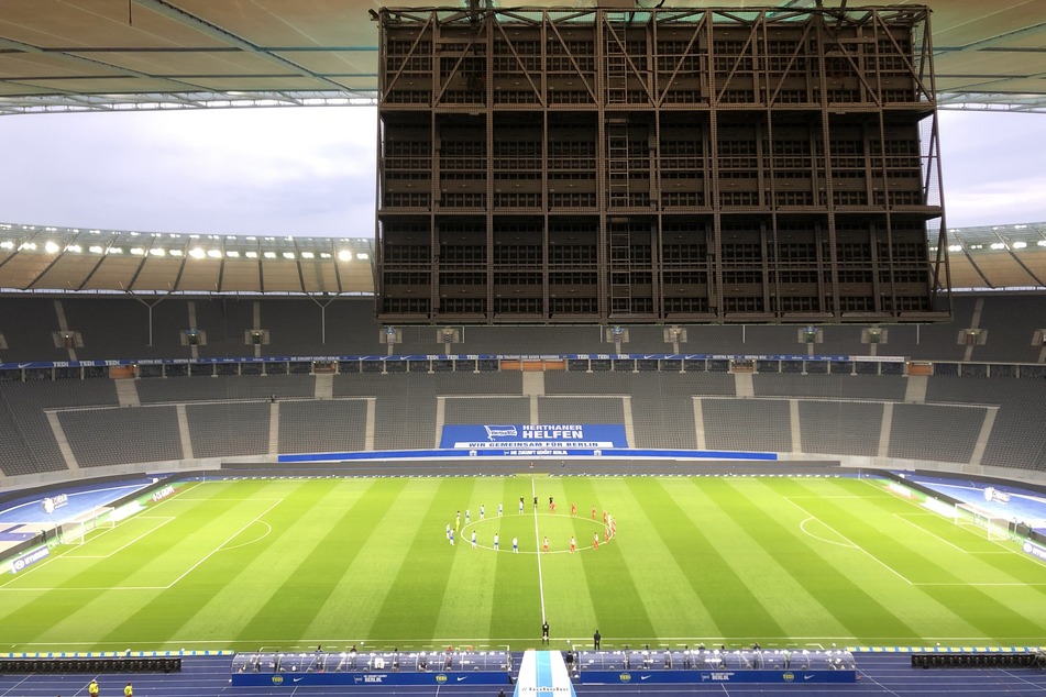 Die Spieler von Hertha BSC und 1. FC Union Berlin stehen auf dem Spielfeld im leeren Stadion
