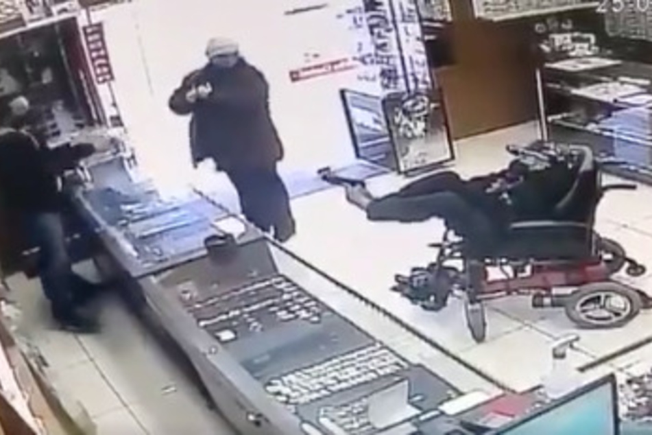Der 19-Jährige richtet mit seinen Füßen eine Waffe auf den Verkäufer hinter dem Tresen.