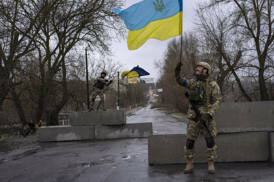 Mit Stolz schwenken diese zwei Soldaten an einer Straßensperre in Butscha die Nationalflagge der Ukraine.