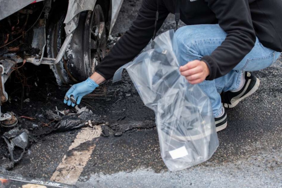 Ein Kriminalbeamter sichert an einem ausgebrannten Fahrzeug Spuren.
