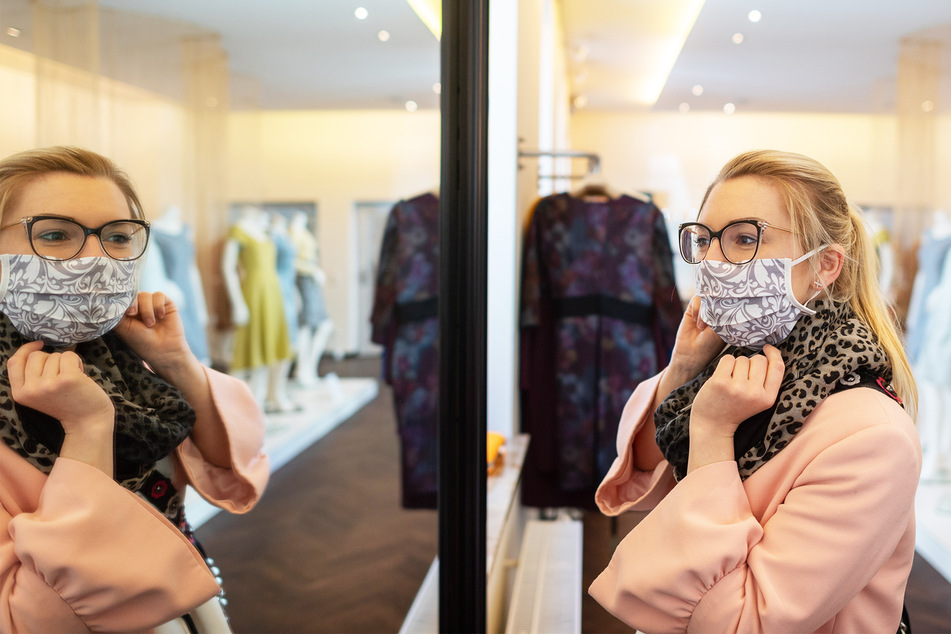 Eine Frau trägt eine Mundschutzmaske beim Einkaufen und schaut in einen Spiegel.