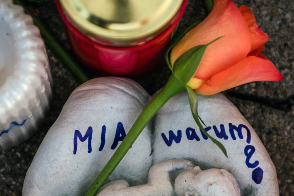 Eine Skulptur in Form zweier Handflächen mit der Aufschrift "Miawarum?" und eine Rose liegen vor dem Tatort (Archivbild).
