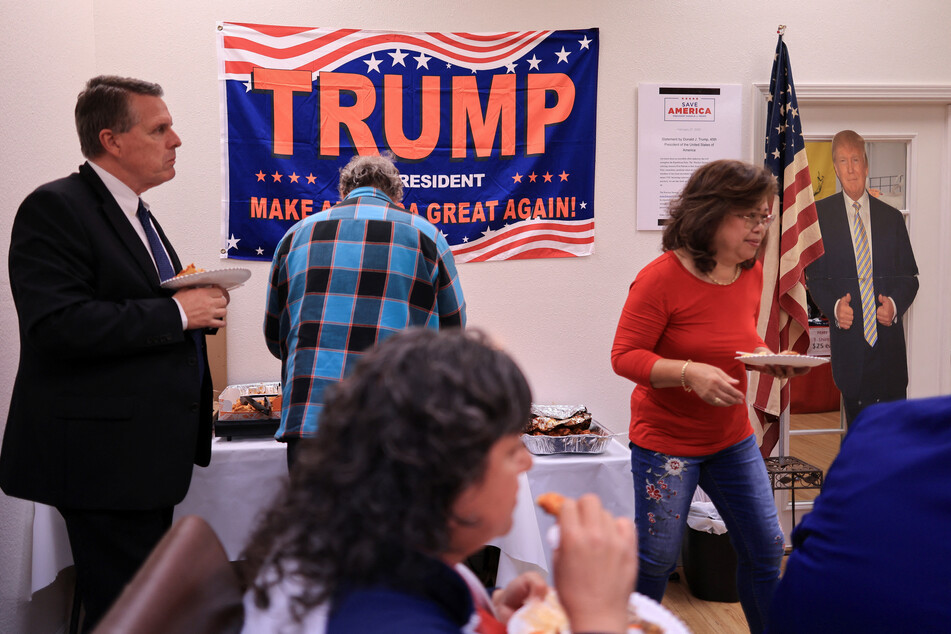 Tim O'Reilly (l.), chairman of the Republican Party Los Angeles, holds a plate with food near a life-size Trump cutout during a Super Tuesday watch party event in Long Beach, California.
