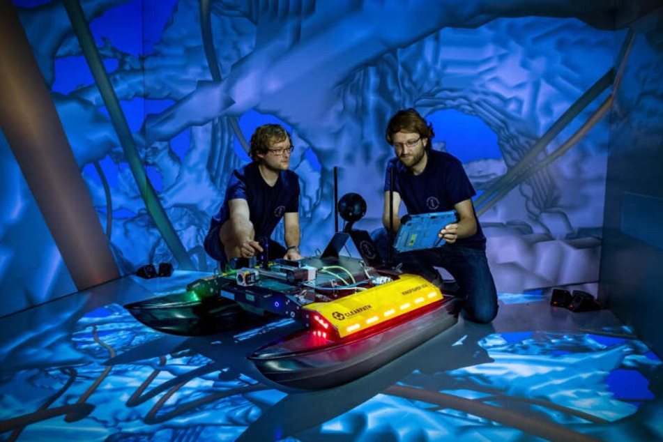 Die TU-Informatiker Robert Lösch (r.) und Mark Sastuba zeigen den neu entwickelten Schwimmroboter „Elisabeth“ in einem Virtual-Reality-Raum.