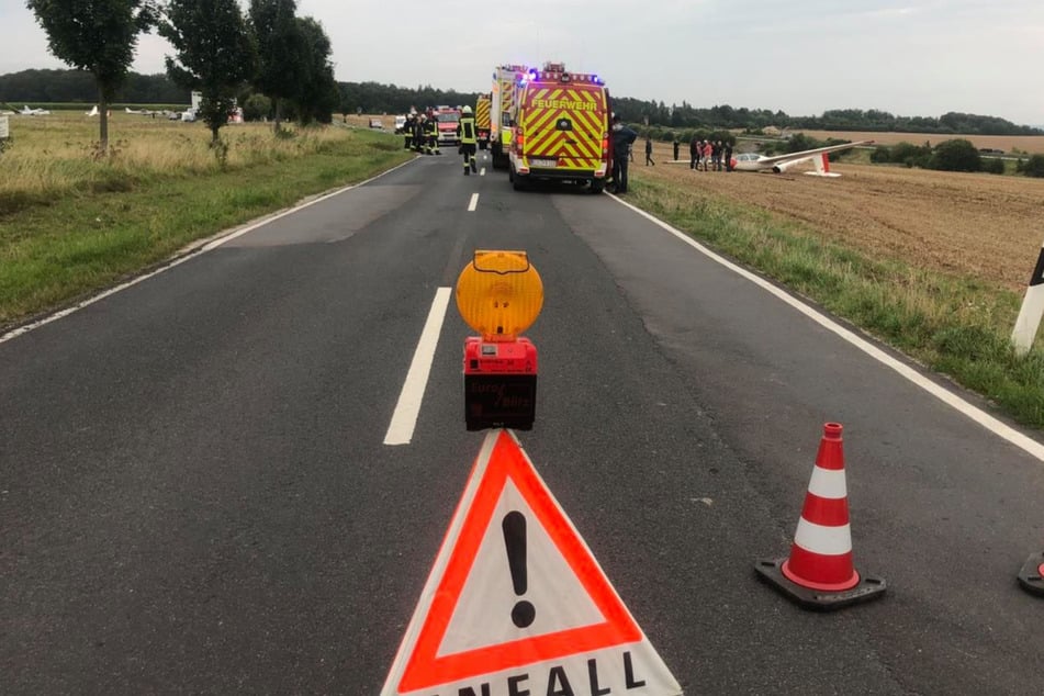 Rettungskräfte sind am Unfallort. Im Hintergrund ist der abgestürzte Flieger zu erkennen.