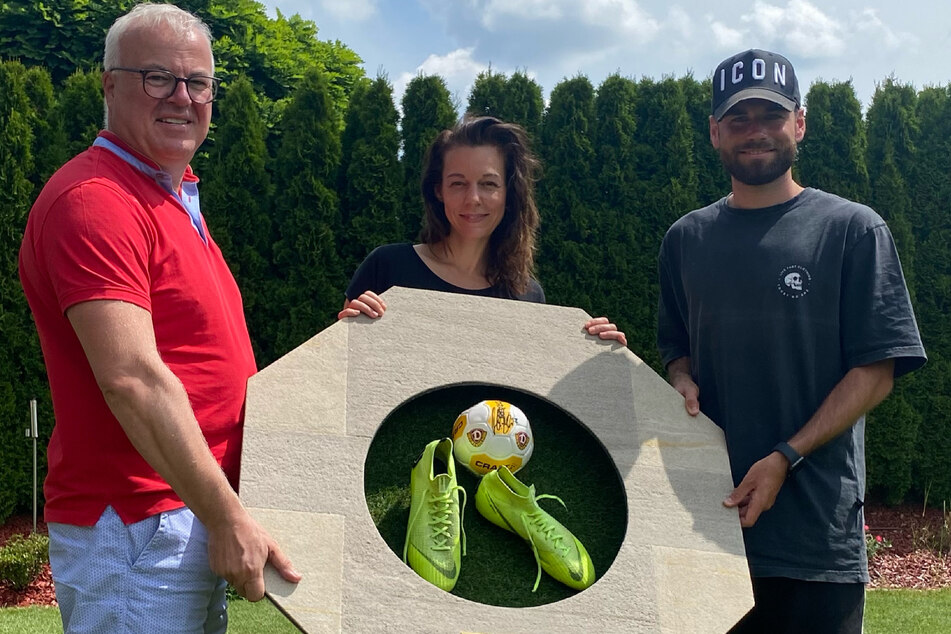Frank Schröder (52, v.l.), Mirjam Köfer (47) und Kicker Niklas Kreuzer (28) zeigen das Wandobjekt, das bei eBay versteigert wird.