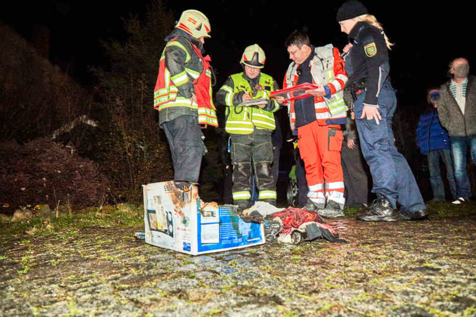 Feuerwehr, Polizei und Rettungsdienst stehen vor dem ausgebrannten Karton.