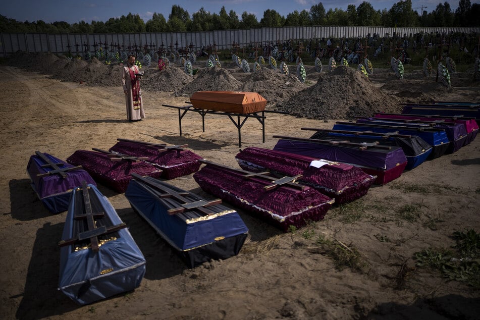 Bei einer Beerdigung segnet ein Priester Särge mit nicht identifizierten Zivilisten, die während der russischen Besatzung in Butscha von den russischen Truppen ermordet wurden