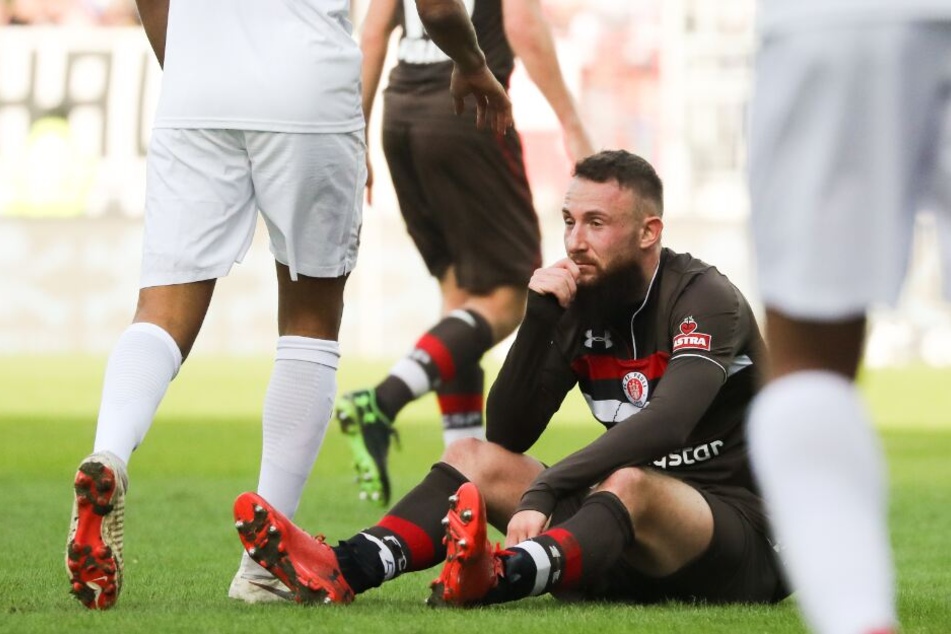 Paulis Marvin Knoll sitzt auf dem Rasen zwischen Spielern von Erzgebirge Aue.