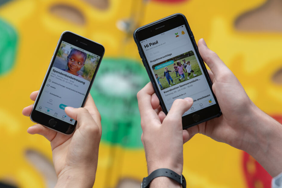 Die beiden App-Entwickler Ludwig Petersen und Paul Bäumler halten zwei Mobiltelefone mit ihrer selber entwickelten App auf dem Display in den Händen.