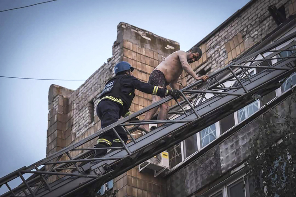 Rettungskräfte evakuieren Menschen aus einem beschädigten Gebäude nach Raketeneinschlägen.