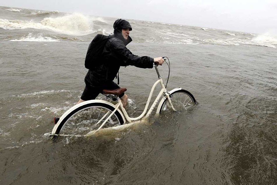 Tyler Holland schiebt sein Fahrrad durch Wasser, das durch Tropensturm "Barry" aus dem Lake Pontchartrain über den Damm geschoben wurde.