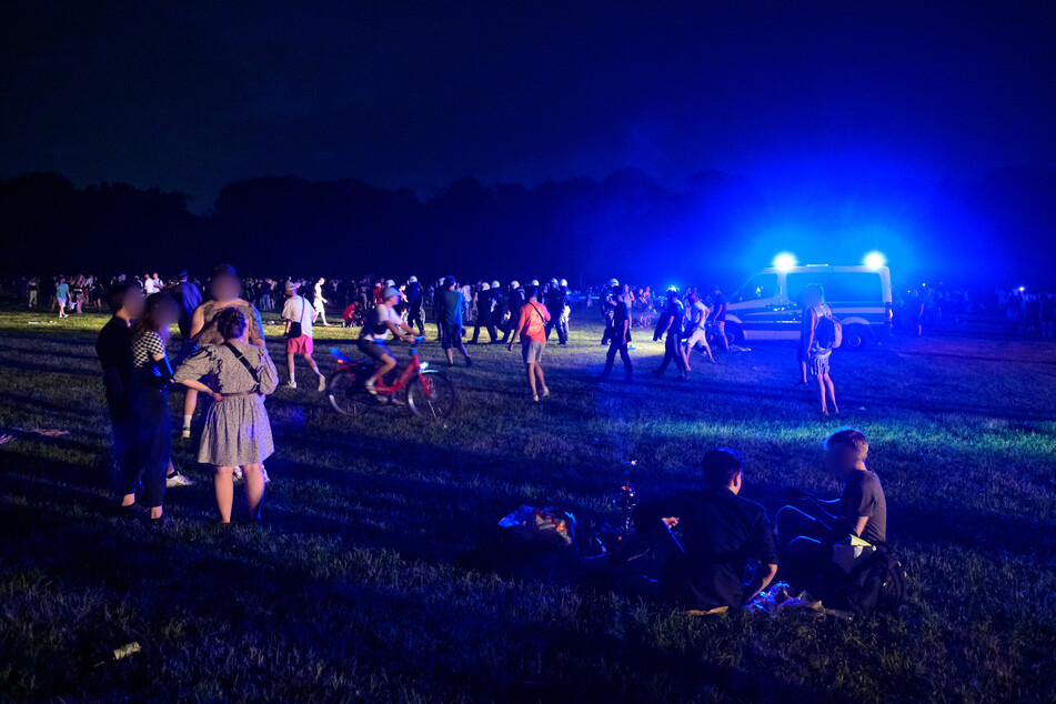 Hamburg: Behelmte Polizisten laufen begleitet von einem Mannschaftswagen mit Blaulicht durch die Menschengruppen auf der Stadtpark-Wiese.