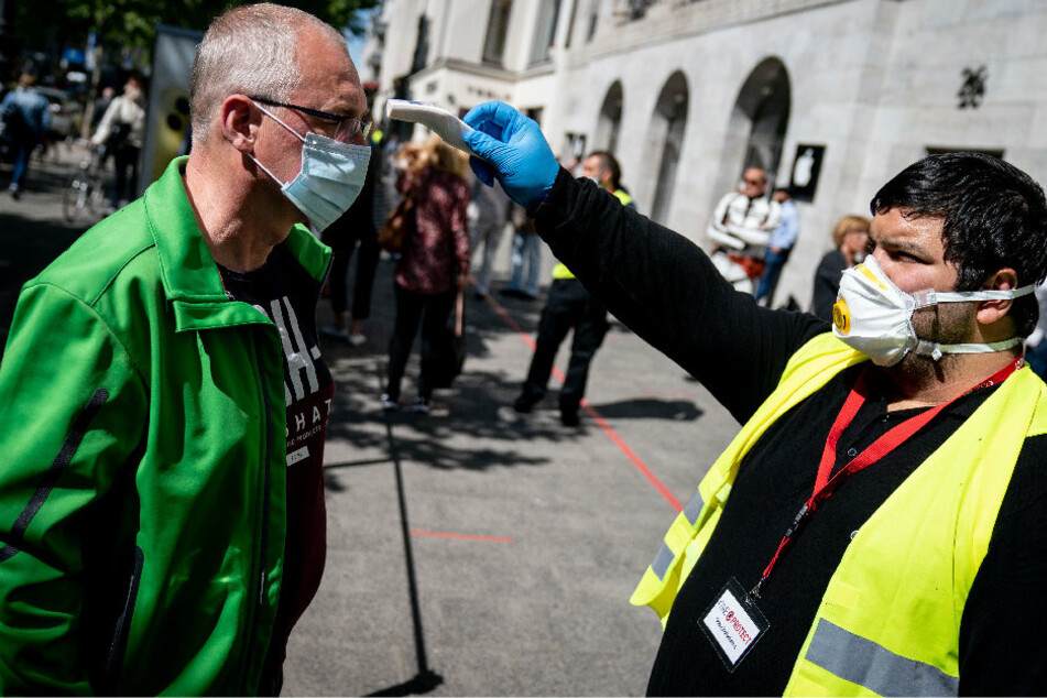 Ein Mitarbeiter misst vor dem Applestore am Kurfürstendamm die Temperatur eines Kunden, bevor dieser das Geschäft betreten darf.