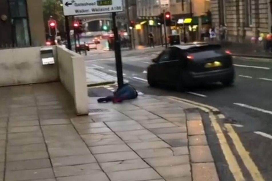 Der Mann knallt gegen ein Straßenschild und bleibt einen Moment liegen. Dann erhebt er sich. Scheinbar nicht schwer verletzt.