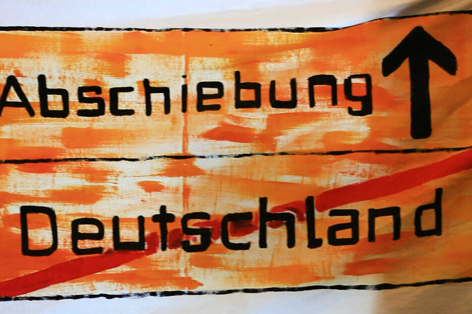 Ein Protest-Transparent "Abschiebung - Deutschland" hängt bei einer Pressekonferenz in einem Fenster. (Archivbild/Symbolbild)
