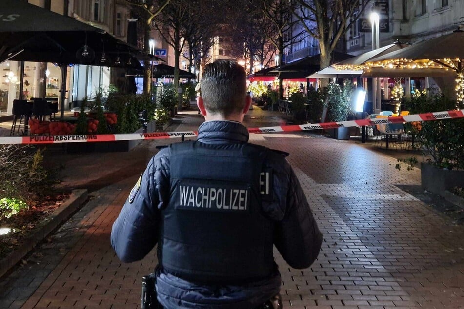 Ein Mitarbeiter der Wachpolizei steht an einem Absperrband in der Innenstadt.