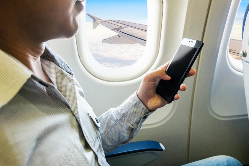 Ein Mann nutzt sein Handy im Flugzeug (Symbolbild).