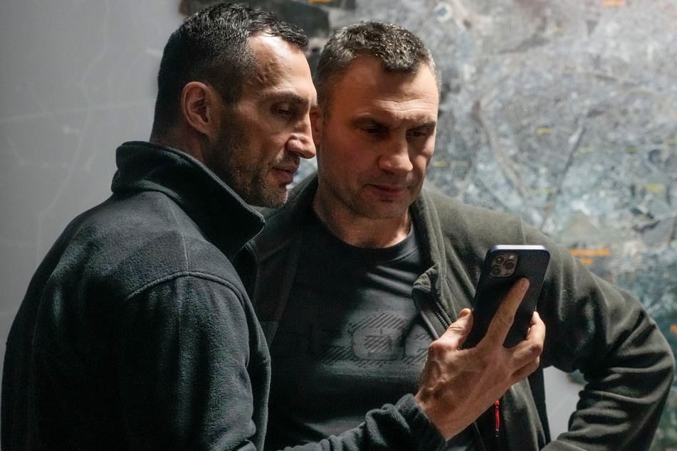 Vitali Klitschko (r.), Bürgermeister von Kiew und ehemaliger Box-Profi, und sein Bruder Wladimir Klitschko, ebenfalls ehemaliger Box-Profi, schauen auf ein Smartphone im Rathaus in Kiew. Russische Truppen haben den erwarteten Angriff auf die Ukraine gestartet und drangen in die Hauptstadt vor.
