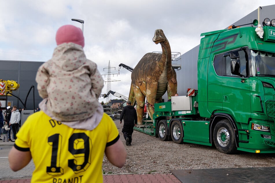 Entlang der Strecke verfolgten zahlreiche Schaulustige den Dino-Transport, allein beim Start waren es rund 30 Menschen. Am Ziel auf dem Gelände der Waschanlage warteten weitere Besucher, darunter viele Eltern mit Kindern.