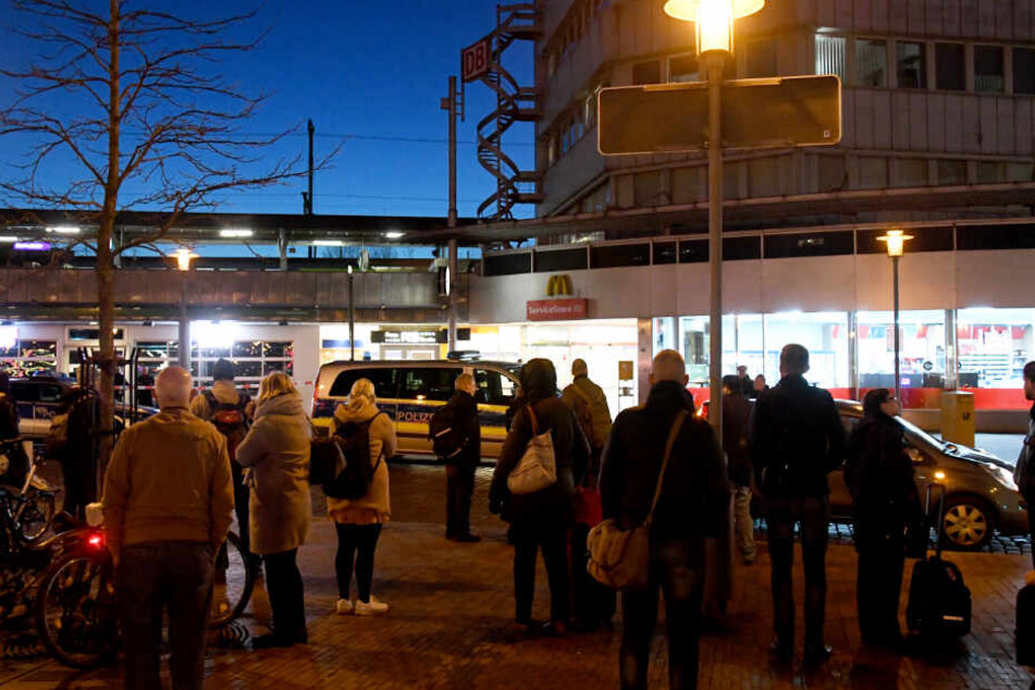 Reisende stehen vor dem Bahnhof Neumünster, da er wegen einer Bombendrohung geräumt wurde.